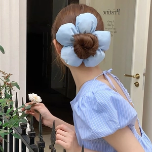 Detail of oversized light blue fabric flower hair tie worn on a bun hairstyle outdoors