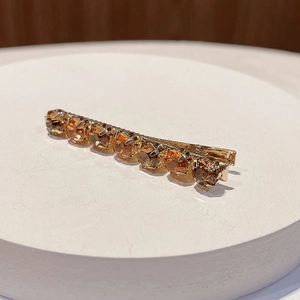 Close-up of golden metal hair clip with sparkling amber faceted crystals on white base