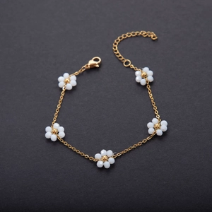 Detail of gold chain bracelet with five white beaded flowers and lobster clasp
