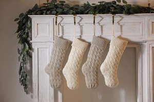Close-up of four cream and beige cable knit Christmas stockings hanging on a cozy fireplace