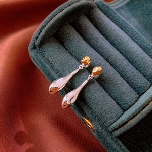 Macro shot of gold and silver teardrop earrings on a luxury velvet jewelry stand