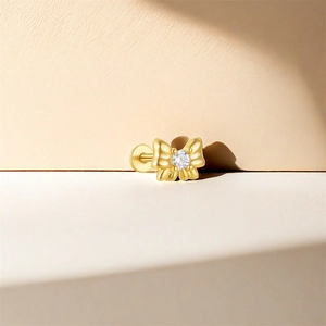 Detail of s925 silver bow stud earring with a central clear zircon on warm geometric background
