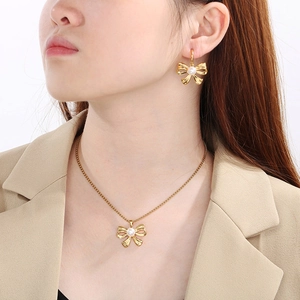 Close-up of gold bow pendant necklace and matching pearl earrings on female model