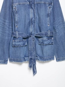 Close-up of blue denim jacket showing waist belt, dual pockets and raw hem texture