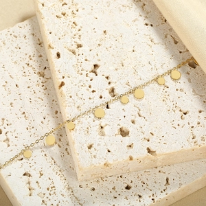Detail of minimalist gold chain necklace with polished round disc pendants on stone