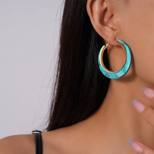 Close-up of gold hoop earrings with turquoise resin inlay on a female model