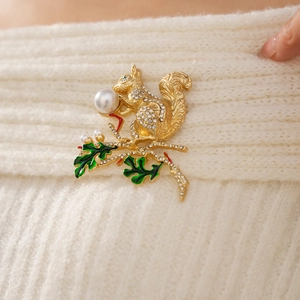 Détail d'une broche écureuil avec perle blanche et feuilles vertes sur un pull en maille