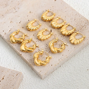 Golden titanium steel twist hoop earrings set on a minimalist travertine display stand