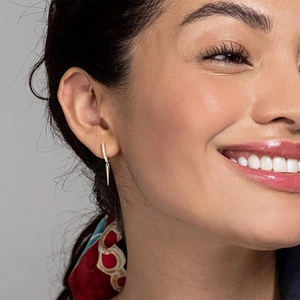Close-up of gold-plated hoop earrings with zircons and triangular cone pendants on model