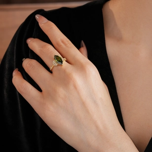 Dettaglio di un anello dorato con pietra verde taglio marquise e piccoli diamanti laterali