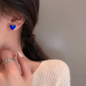 Detail of Klein blue heart earrings and silver chain ring on model wearing white sweater