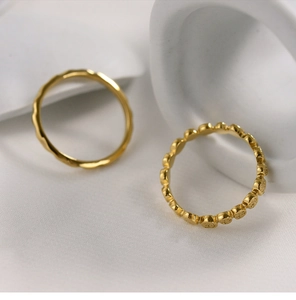 Detailed macro view of gold-plated honeycomb and wavy stackable rings on white silk