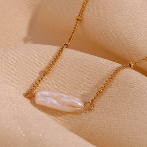 Detail of baroque pearl pendant on a gold beaded necklace over champagne fabric