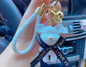 Close-up of white resin bear keychain with woven strap and golden bell detail