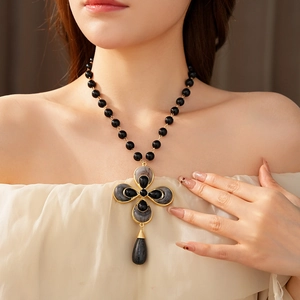 Detail of vintage flower teardrop cross necklace with black beads and gold-tone metal