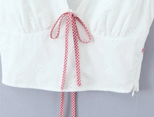 Detail of white V-neck top featuring red plaid tie and delicate floral hollow embroidery