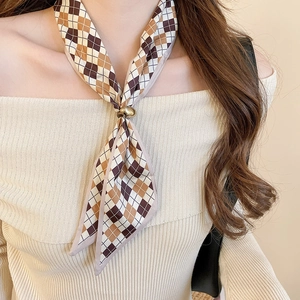 Detail of a brown diamond pattern silk scarf with a gold ring buckle on a beige sweater