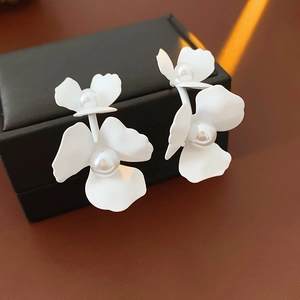 Detailed close-up of matte white C-shaped flower earrings with center pearl accent