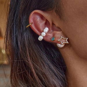 Star-shaped earrings with large pearls and blue gem studs on a model's ear