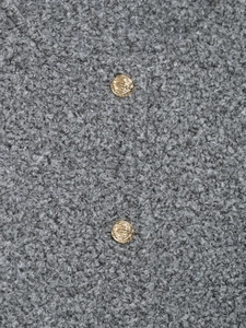 Detail shot of grey bouclé fabric texture with a decorative gold textured metal button