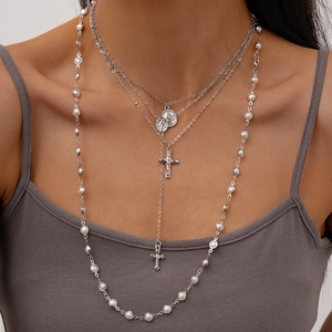 Detail of layered silver necklaces featuring faux pearls, cross and oval medal pendants