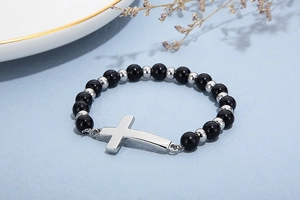 Détail d'un bracelet de perles noires avec un pendentif croix en argent sur tissu texturé