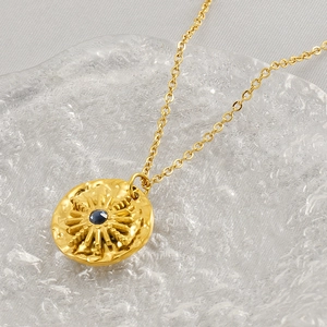 Detail of gold starburst medallion necklace featuring a central deep blue gemstone