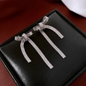 Elegant silver bow earrings with woven mesh tassels on a dark premium display stand