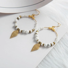 Macro shot of gold hoop earrings with white marble beads and textured rhombus charms