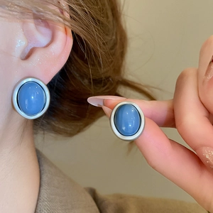 Close-up of minimalist oval stud earrings in grey-blue resin and matte silver frames