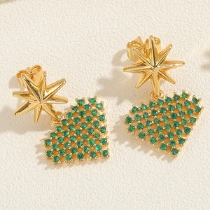 Macro shot of gold octagonal star and green zircon heart earrings on textured background