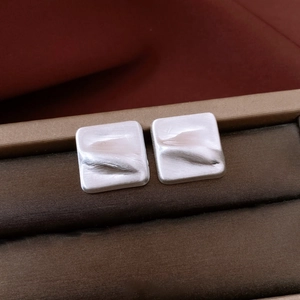 Vue macro des boucles d'oreilles carrées argentées avec texture ondulée 3D sur boîte
