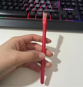 Close-up of a square angled brow brush with a red handle held against a backlit keyboard