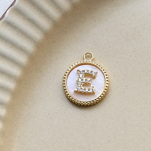 Macro view of gold plated round letter E shell pendant inlaid with zircon crystals