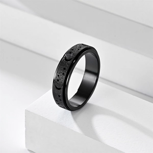 Close-up of black matte spinner ring with moon and star engraving on white stand