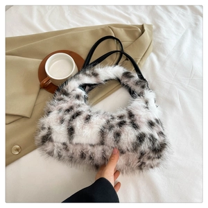Flat lay of a plush cow print crescent handbag with black leather strap on a blazer