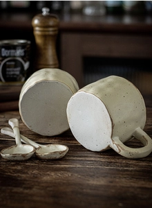 Close-up of handmade beige ceramic mugs and spoons with vintage brown speckled glaze