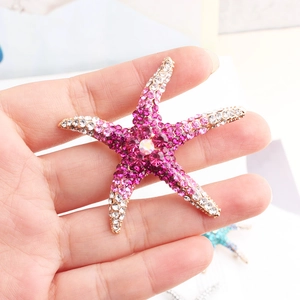 Close-up of hand holding a starfish brooch with pink and white rhinestones