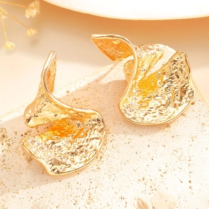 Detail of gold fan-shaped earrings with lava texture on natural stone background