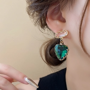 Details von Goldohrringen mit rosa ovalen Steinen und grünen herzförmigen Kristallanhängern