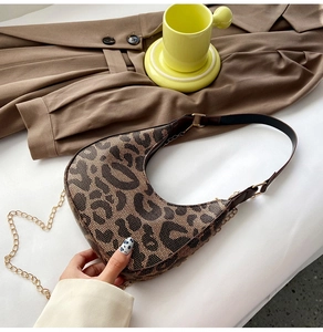 Detail of leopard print crescent bag with leather strap and golden chain on a white desk