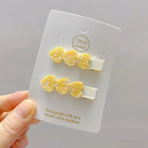 Detail of yellow glitter heart hair clips for girls on a white handmade display card