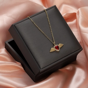 Close-up of gold heart pendant with red ruby and wings on pink silk backdrop
