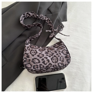 Détail du sac lune léopard avec bandoulière froncée et nœud sur fond en tissu blanc