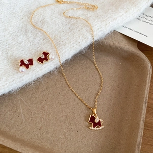 Detail of gold horse necklace and pearl earrings set on a wooden display tray