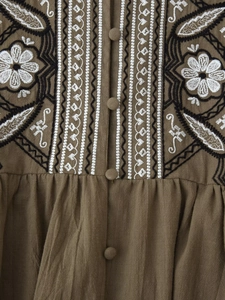 Detail of floral embroidery and cloth-covered buttons on brown linen shirt fabric