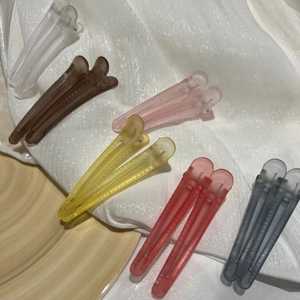 Assorted colorful matte duckbill hair clips scattered on a soft white textured fabric