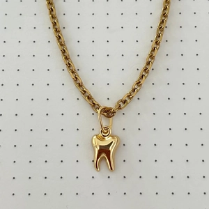 Macro shot of gold tooth pendant necklace with thick chain link on dot pattern background