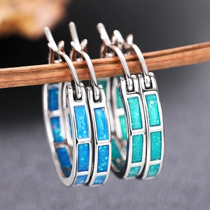 Dettaglio di orecchini a cerchio in argento con opale blu su un ramo di legno rustico