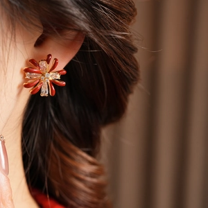 Close-up of red flower stud earring with cubic zirconia on model wearing gold jewelry